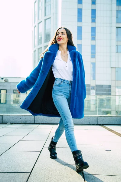都市の背景にポーズの青い毛皮のコートの若い女性 — ストック写真