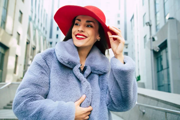 通りを歩いて灰色の毛皮のコートと赤の帽子の若い女性 — ストック写真