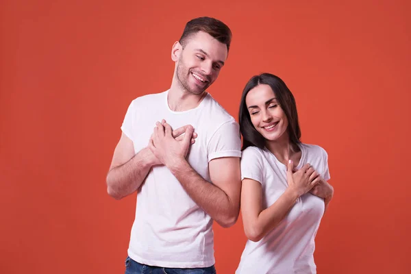 Beautiful young cute couple in love in white t-shirts holding them hands on chest