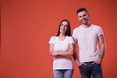 Güzel genç bir çift beyaz boş t-shirt turuncu arka plan üzerinde poz olan. İlişki, Aile, reklam