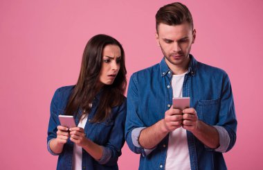 Akıllı telefonlar içinde rahat kıyafet tutan pembe arka plan üzerinde izole duran genç çift