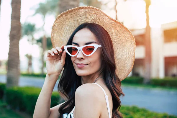 Brave new world. Splendid peaceful girl with rosie lips and slight smile is fixing her red & white sunglasses with thin fingers.