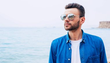 Gökyüzü müttefikiydi. Güzel çocuk kot gömlek ve güneş gözlüğü, koyu saç ve sakal ile gökyüzü ile deniz nerede bağlanma noktası güzellik yoluyla izliyor.