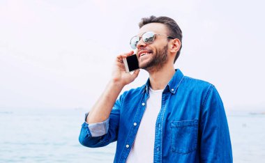 Hoş bir adam yüzünde çarpıcı gülümseme o telefon görüşmesi yüzünden sevgilisiyle memnun onun ruh halinde olduğunu gösteriyor. T-shirt ve kot gömlek onun kıyafeti oluşur.