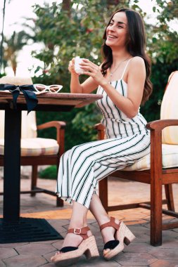 Çay vakti! Beamish kız çayını tarafından ahşap masa yaşıyor. Güzelliği güzel bir siyah, beyaz ve kahverengi renk kıyafet uygun ve Aksesuar eşleme ile eşlik ediyor.