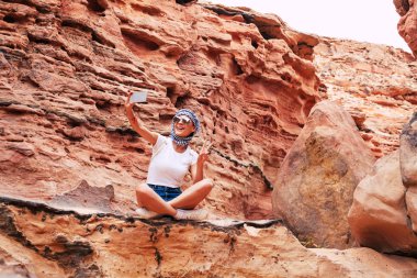 Şanlı belirsizlik. Kız büyük rock yakınındaki bir barış işareti telefonunu kameraya gösteriyor. Onun tişört, şort ve atkı mükemmel atmosferi eşleşir.