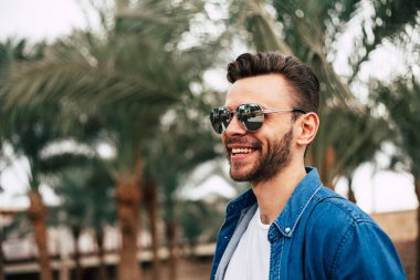 Genç adam arka plan avuç içi ile güneş gözlüğü takıyor gülümseyen