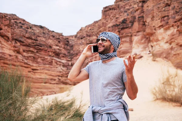 クーフィーヤと砂漠のシーンで電話で話しているサングラスを身に着けている旅行者 — ストック写真
