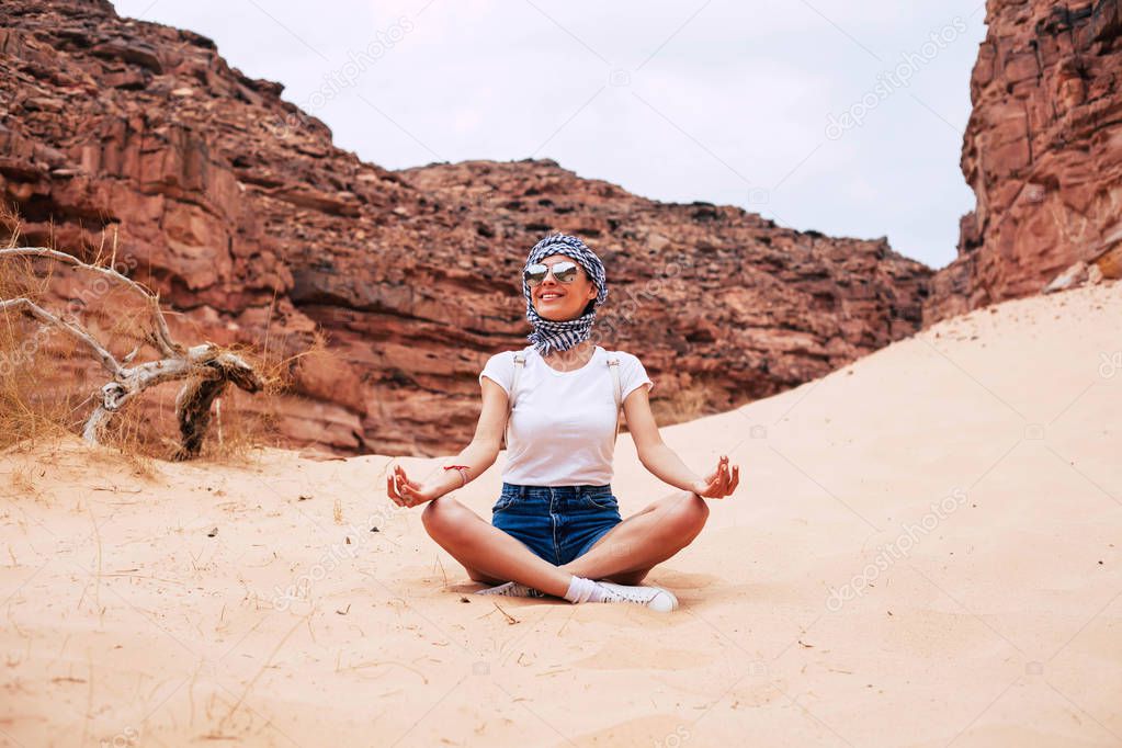 Meditation of life. Girl in a cheered-up mood is meditating among grand rocks, sand and immense clear sky. Her outfit of t-shirt, shorts and sneakers  allows to move freely.