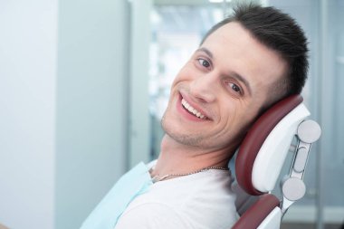 Estetik stomatology. Yakışıklı dişçi sandalyede yüzünde göz alıcı gülümseme ile diş hekimi çalışma sonuçları ile baktıktan sonra harika ve mutlu hisseder.