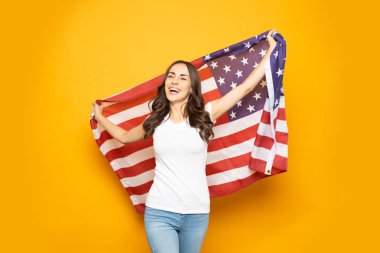Amerikan rüyası. Denim kot ve beyaz uzun kıvırcık saçlı hilariously güzel kız t-shirt yanan sarı arka plan önünde Amerikan bayrağı ile yürüyor.