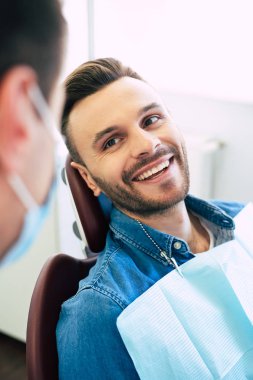 Pretty face mimic and a white smile of a nice man in a dental chair after getting a doctors treatment  in a professional clinic. clipart