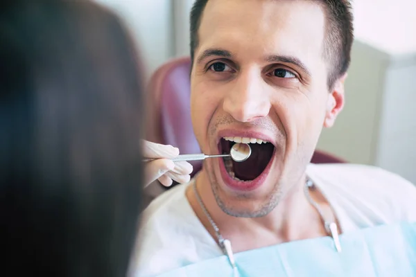 Stress- free treatment. A dentist of a dental clinic is using a dental mirror to make an examination of condition of patients teeth who is sitting right in front of she.