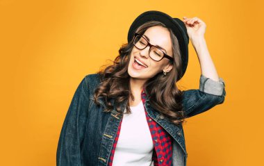 Serin genç hipster kadının yanında baharatlı orange arka plan şapkasını, o Kot ceket gömlek ve temel beyaz T-shirt üzerinde giyinmiş ve aksesuarları ile birlikte sabitleme.