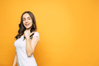 Eğlenceli bir görünüm. Uzun kahverengimsi kıvırcık saç ile Bodacious kız, ışık T-shirt giyen ve gibi gösteren canlı turuncu arka plan yakın ela gözleri ve parlayan cilt.