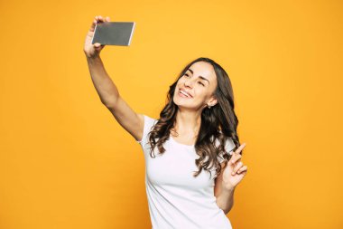 Git başımdan. Aurantiaceous arka planda yakın Smiley genç kadın bir yandan onun telefon tutarak ve bunun bir yardımı ile bir selfie yapıyor.