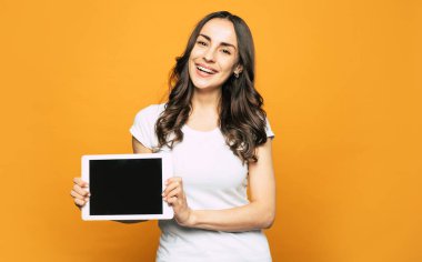 İşte burada! Samimi kahverengi gözleri olan bir kız, canlı turuncu arka planda yakın koyu kahverengi dalgalı uzun saç onun zarif ellerde bir tablet PC tutuyor.