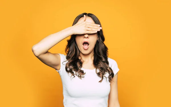 Wow! An elegant girl with shiny hair near the flamboyant background is using her hand to close her eyes because she saw something scared.