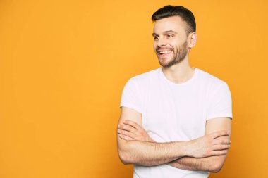 Kahverengi saçlı ve sakallı bir adamın göz alıcı gülümseme, temel beyaz t-shirt göğüs elleri ve giysi geçti