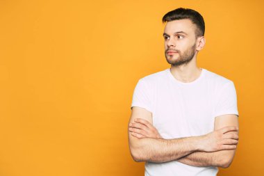 Bir sakal, kalın parlak saçları ve turuncu duvarın yanında büyük koyu kahverengi gözleri ile yan dan rahat kıyafetli Adam