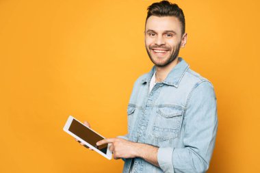 Sarı arka plan üzerinde elinde modern tablet ile rahat iş adamı yan görünüm portresi