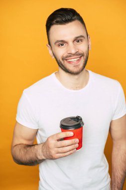 Sarı arka plan üzerinde elinde fincan ile beyaz t-shirt yakışıklı genç adam.