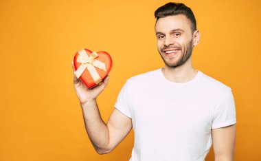 Yakışıklı mutlu genç adam elinde kalp şeklinde hediye kutusu tutar ve kameraya bakar