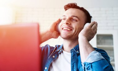 Kulaklık Mutlu güzel modern adam evde dizüstü bilgisayardan müzik dinliyor