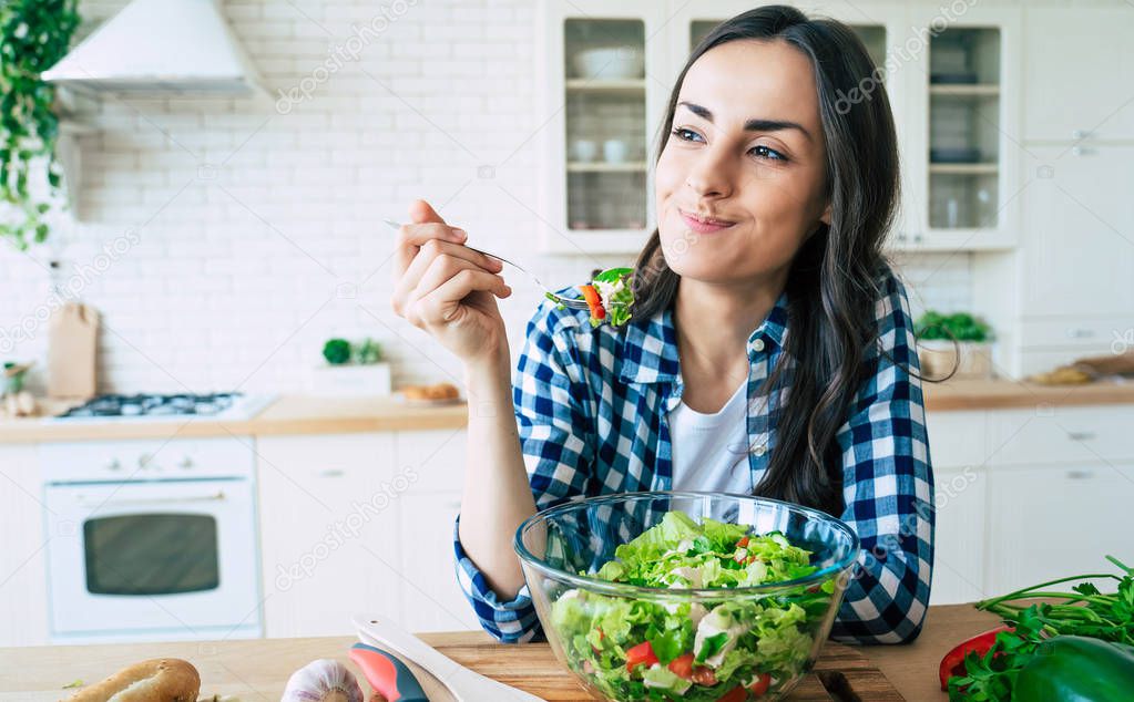 Healthy lifestyle. Good life. Organic food. Vegetables. Close up portrait of happy cute beautiful young woman while she try tasty vegan salad in the kitchen at home.