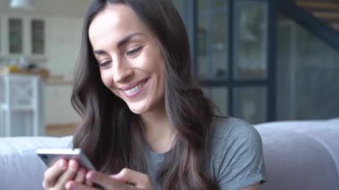 Evde kanepede otururken akıllı telefon tutan gülümseyen esmer kadın