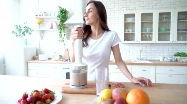 Meyve ile sağlıklı vegan smoothie. Rahat ev giysileri güzel mutlu genç kadın evde mutfakta sebze sütü ve farklı mevsim meyve ile fitness kokteylhazırlanıyor. Sportif yemek