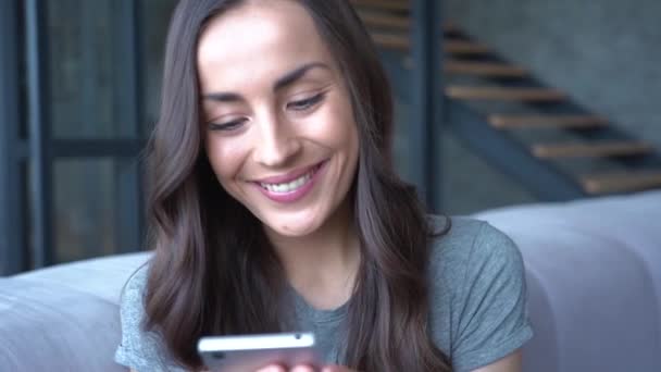 Sorrindo Morena Mulher Segurando Smartphone Enquanto Sentado Sofá Casa — Vídeo de Stock