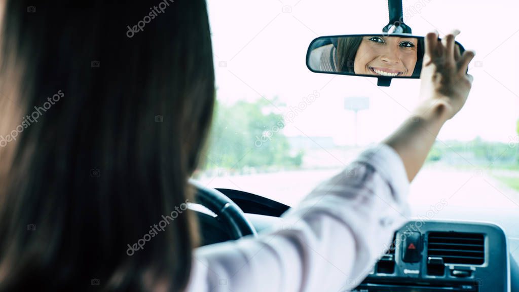 Beautiful female driver adjusting rearview mirror in car