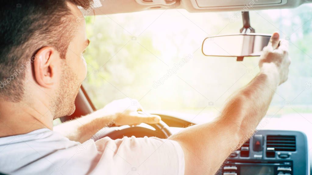 Handsome male driver adjusting rearview mirror in car