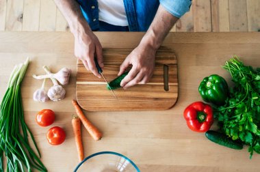Sağlıklı yemek pişiren adam. Kesme tahtasında taze sebzeler var. Yemek pişirme konsepti. Diyet. Sağlıklı ve vegan yaşam tarzı. Evde yemek pişirmek. Yemek hazırla. Erkek elleri mutfakta sebze kesme