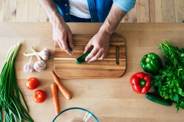 Sağlıklı yemek pişiren adam. Kesme tahtasında taze sebzeler var. Yemek pişirme konsepti. Diyet. Sağlıklı ve vegan yaşam tarzı. Evde yemek pişirmek. Yemek hazırla. Erkek elleri mutfakta sebze kesme