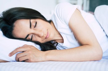 Günaydın. Rahatla ve evde dinlen. Beyaz bir yatakta uyuyan güzel genç esmer kadın.