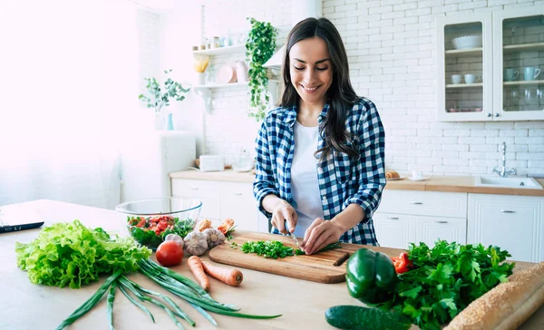 Beautiful young woman is preparing vegetable salad in the kitchen. Healthy Food. Vegan Salad. Diet. Dieting Concept. Healthy Lifestyle. Cooking At Home. Prepare Food. Cutting ingredients on table