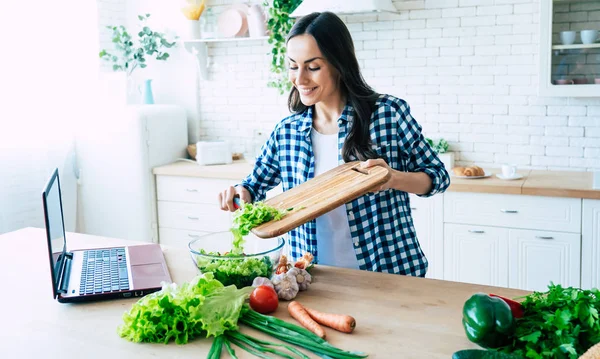 Beautiful young woman is preparing vegetable salad in the kitchen. Healthy Food. Vegan Salad. Diet. Dieting Concept. Healthy Lifestyle. Cooking At Home. Prepare Food. Cutting ingredients on table