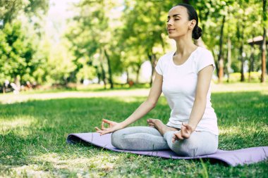 Parkta kadın Yogası. Lotus genç esmer kadın parkta yeşil çim oturan poz. Sakin ve meditasyon konsepti.