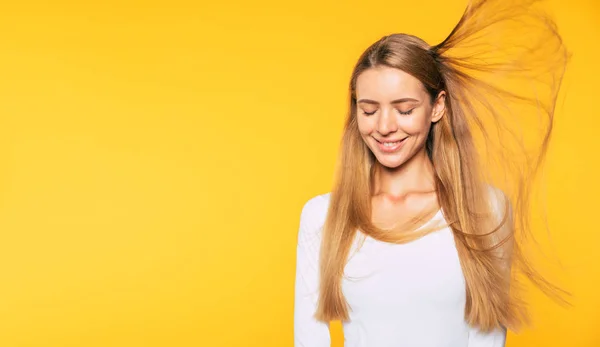 黄色の背景に隔離された飛行ブロンドの髪を持つ魅力的な笑顔の若い女性 — ストック写真