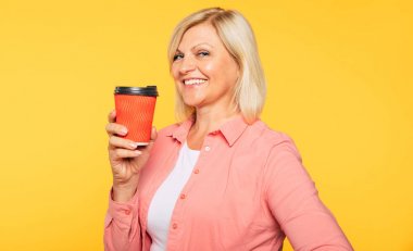 Bayana bir kahve! Elinde kırmızı fincan ile rahat giysiler içinde Mutlu güzel sarışın yaşlı kadın stüdyoda poz olduğunu. Dinlenme zamanı. 