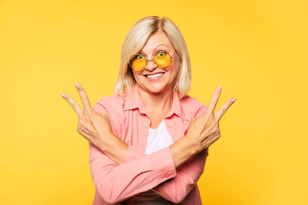 I'm crazy grandma! Excited and emotional beautiful hipster senior woman is posing on yellow background