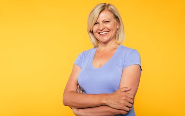 Mutlu gülümseyen güzel sevimli sarışın yaşlı kadın rahat giyim sarı arka plan üzerinde izole güzellik temiz cilt. Sağlık ve kozmetoloji kavramları. Emekli ve olgun insanlar