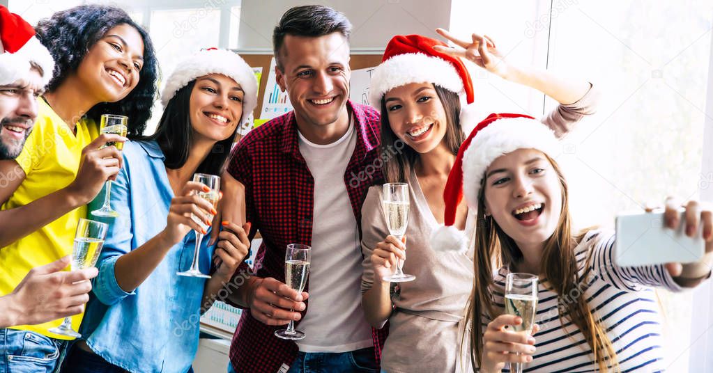 Group of happy multiracial friends celebrating together Christmas and posing for selfie with glasses of champagne