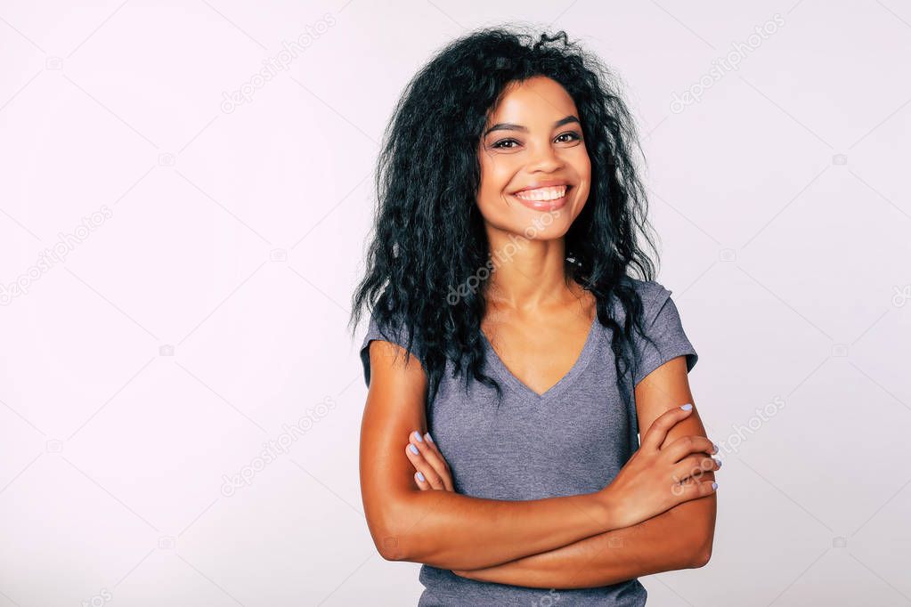 Merry mixed race woman with arms crossed posing on white studio background