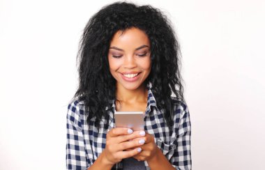 Gözlüklü mutlu ırk kadını elinde akıllı telefonla beyaz stüdyo arka planında mesajlaşıyor.   