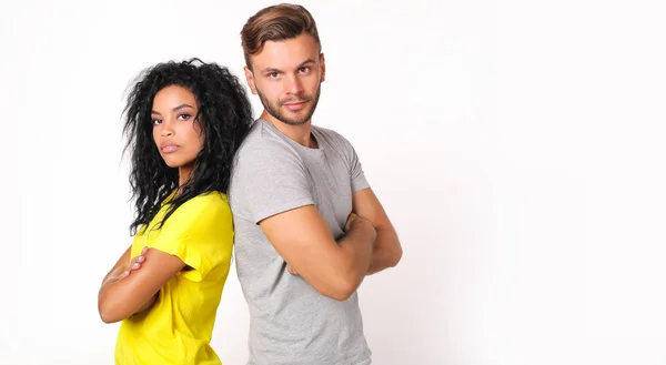 serious couple of friends in casual style standing back to back with crossing arms and looking at camera with proud faces  on white studio background