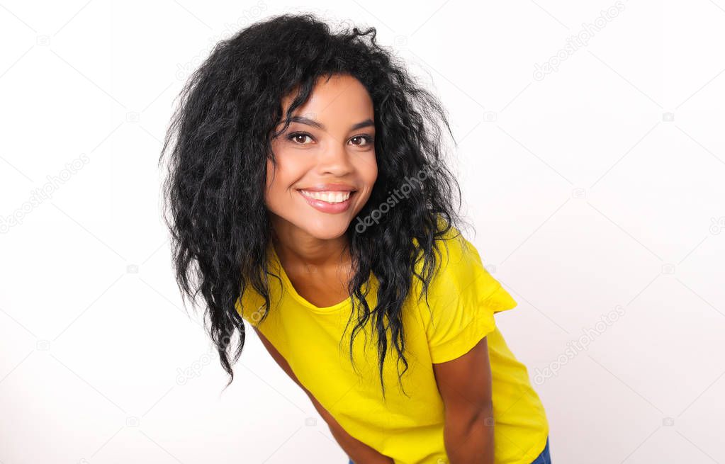 portrait of happy beautiful mixed race woman in bright yellow t-shirt smiling and looking at camera while posing on white studio background 