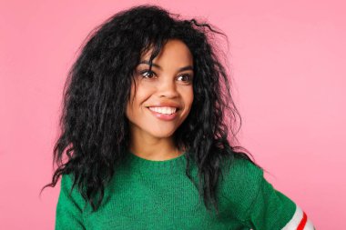 Sıcak yeşil kazak giyen, gülümseyen ve pembe stüdyo arka planına bakan güzel bir kadının portresi. 